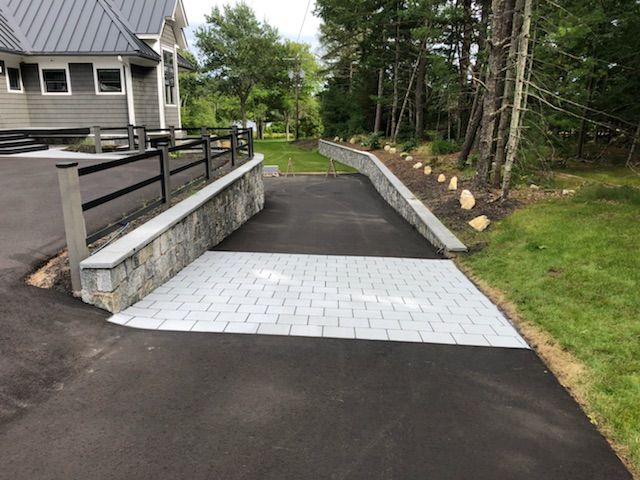 A driveway with a stone wall and a fence leading to a house.