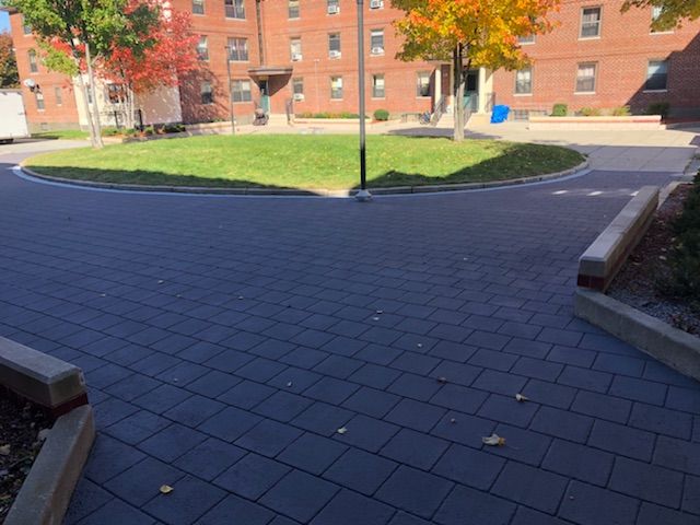 A brick walkway leading to a park with a brick building in the background.