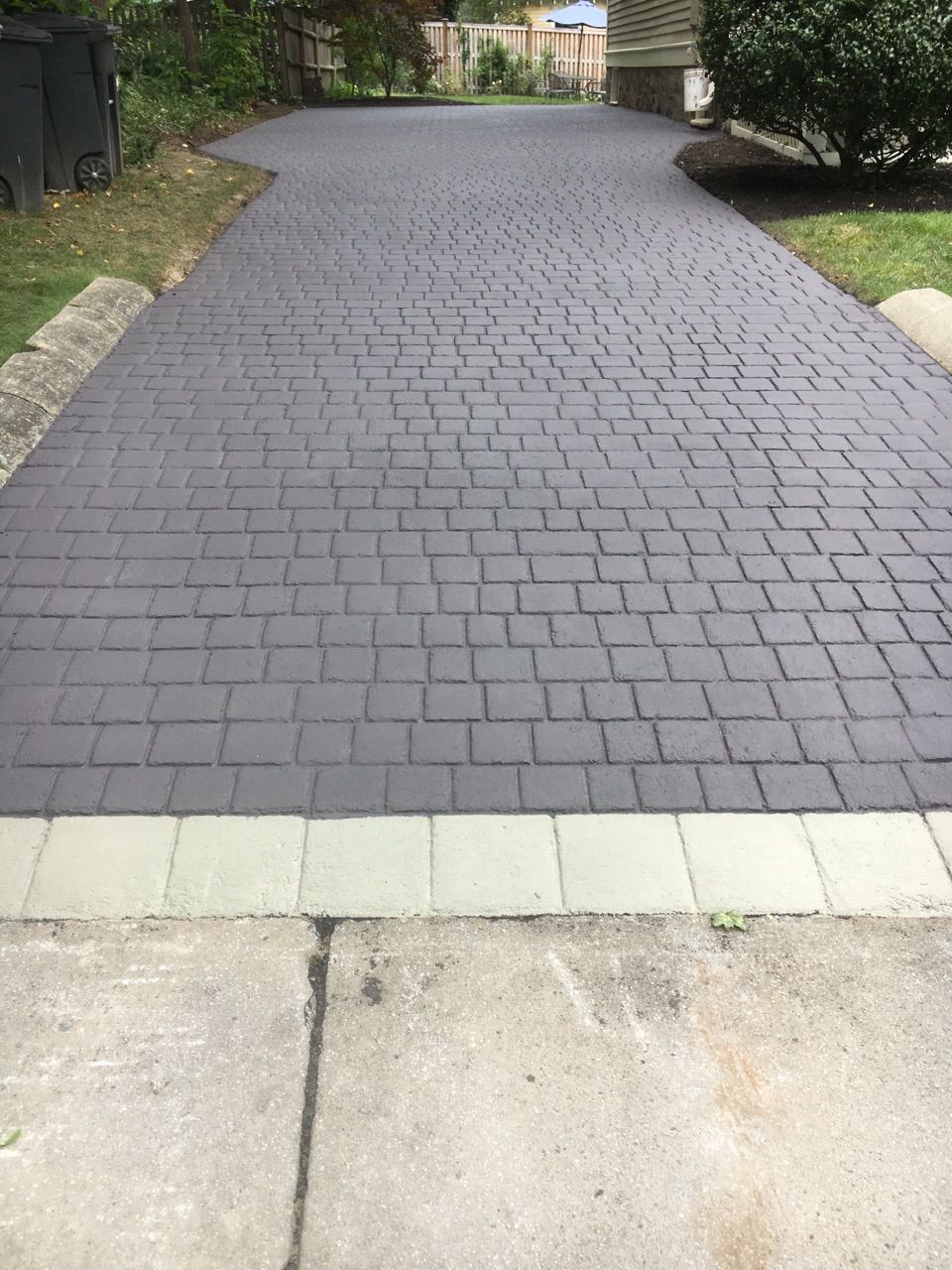 A brick driveway with a white border is leading to a house.