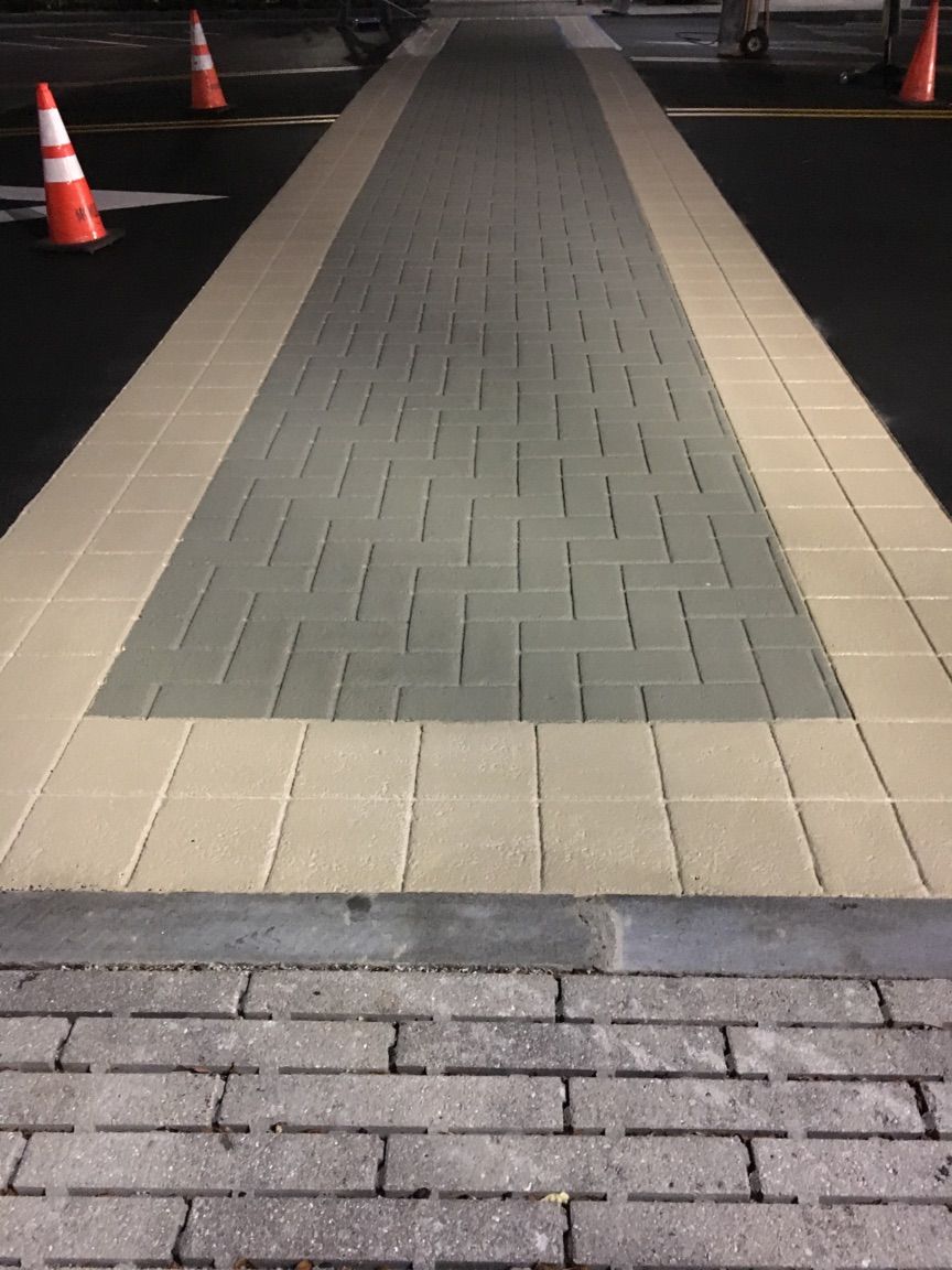 A brick walkway in a parking lot with traffic cones in the background