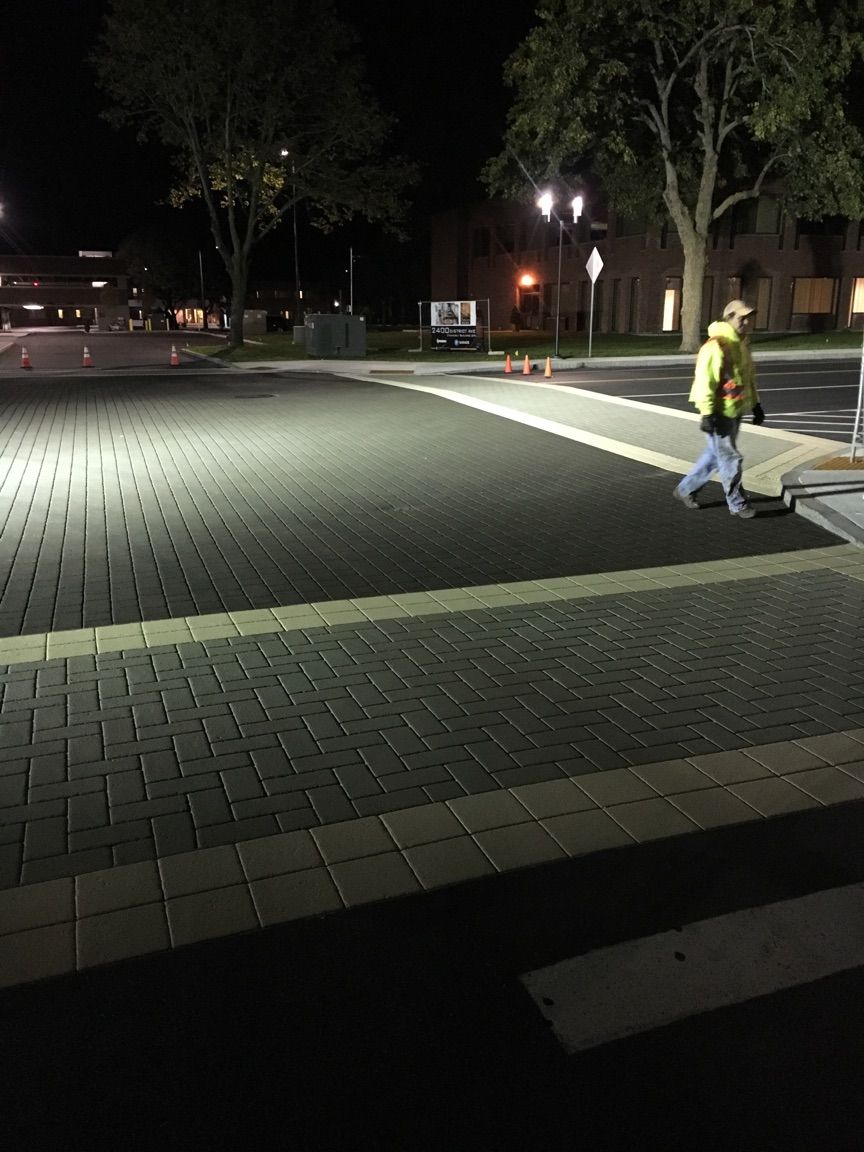 A person is walking across a brick sidewalk at night