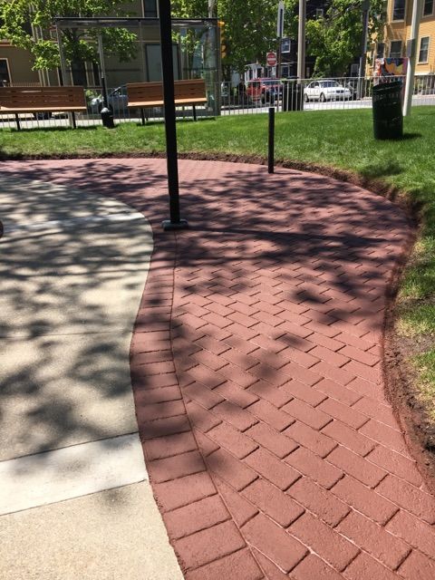 A brick walkway in a park with a bench in the background