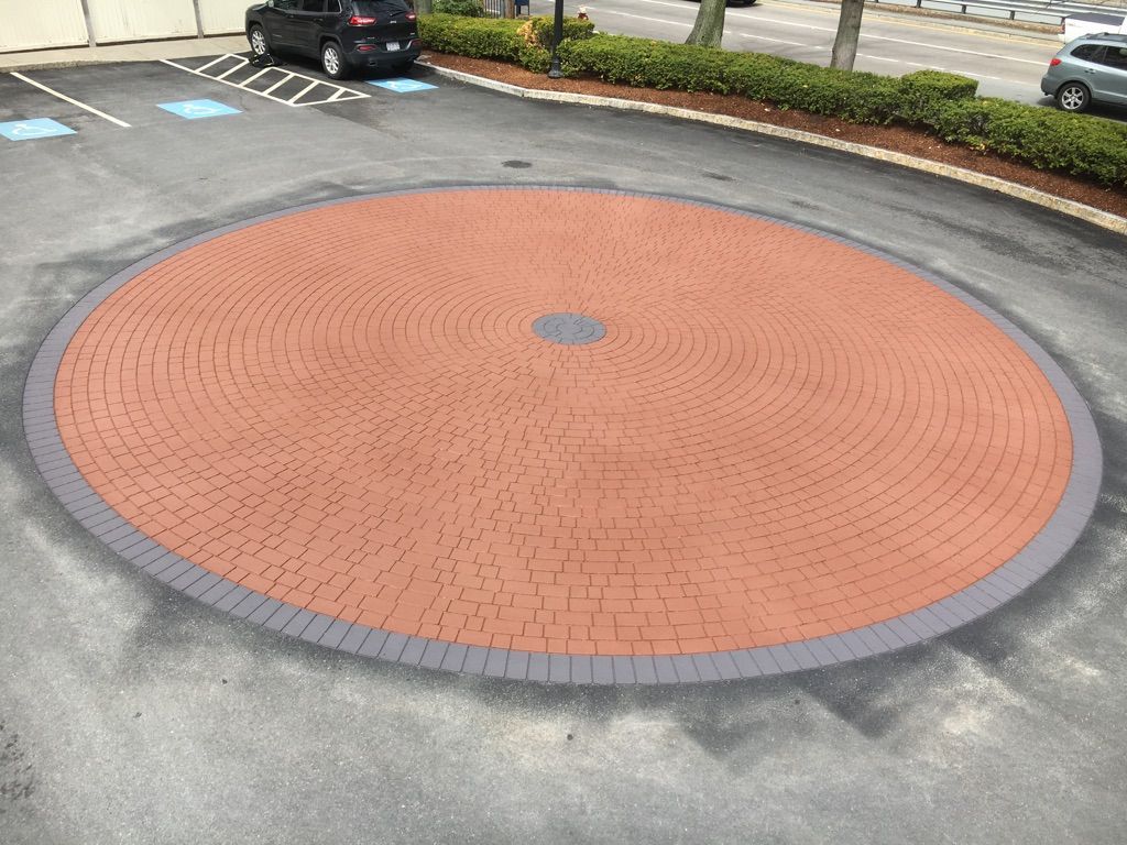 A circular brick pavement in a parking lot with a car parked in the middle.