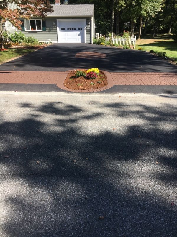 A driveway leading to a house with a flower bed in the middle