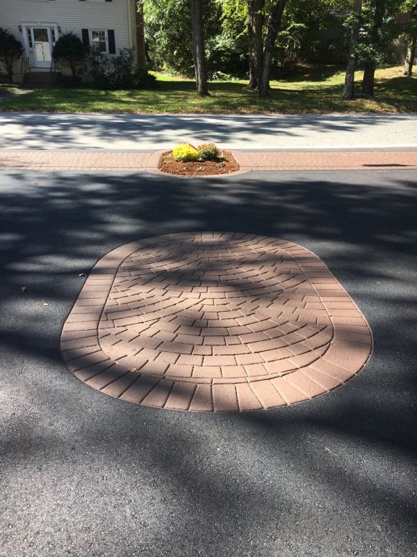 A driveway with a brick circle in the middle of it.