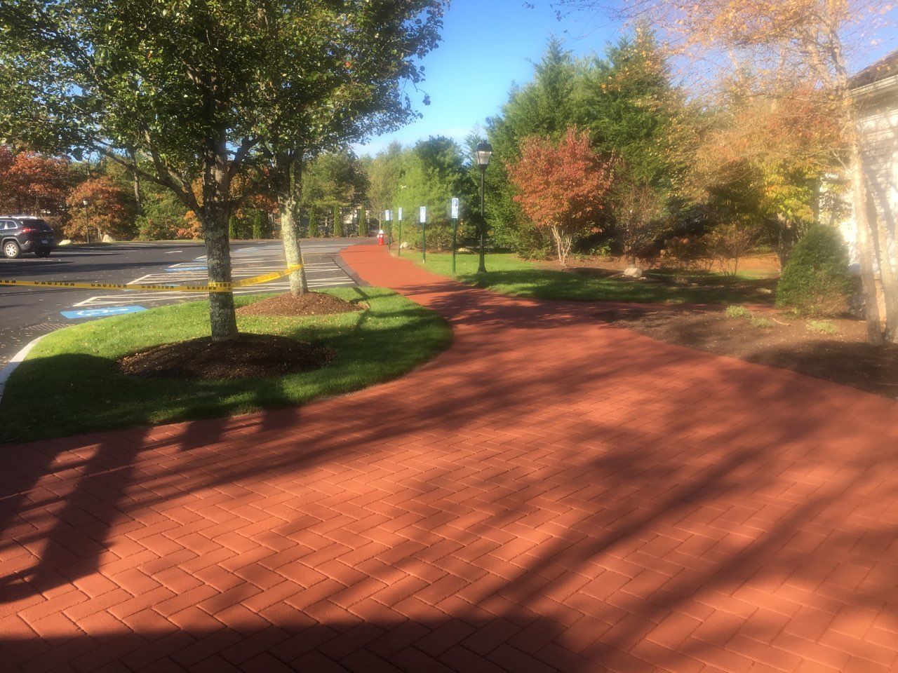 A brick walkway leading to a parking lot with trees in the background