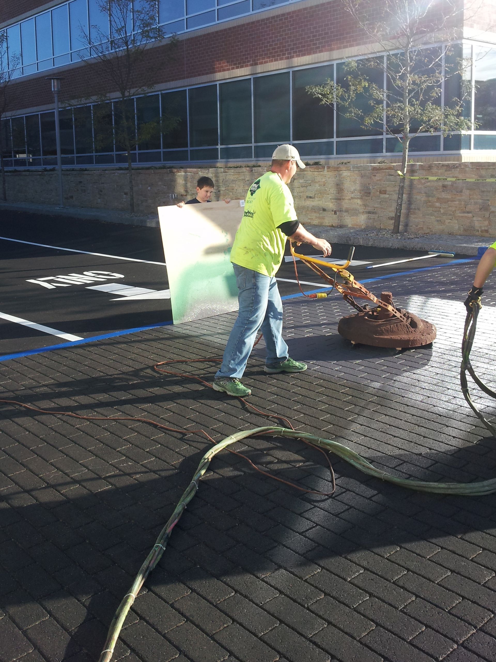 A man in a yellow shirt is cleaning a manhole cover with a hose.