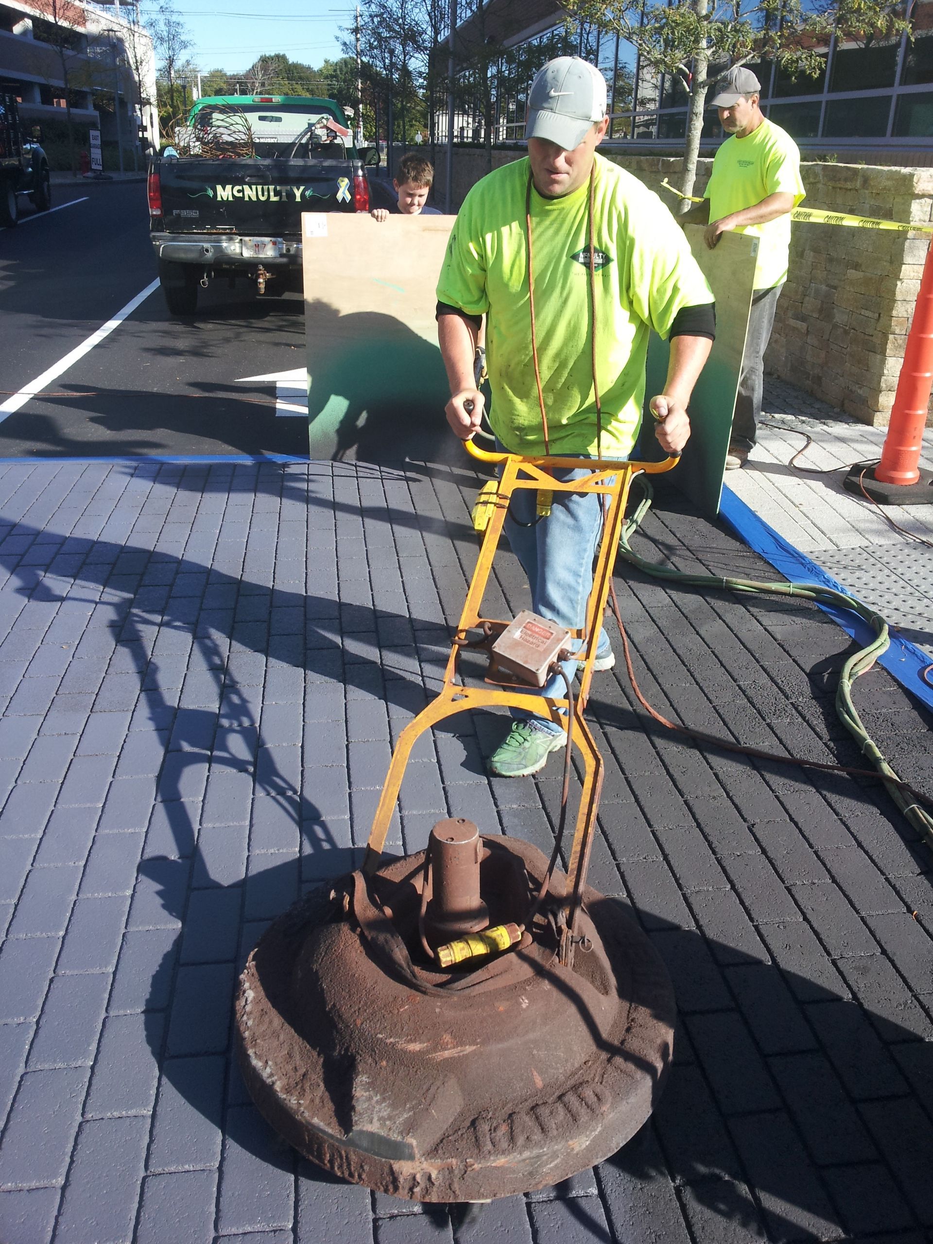 A man in a yellow shirt is using a machine on a brick sidewalk