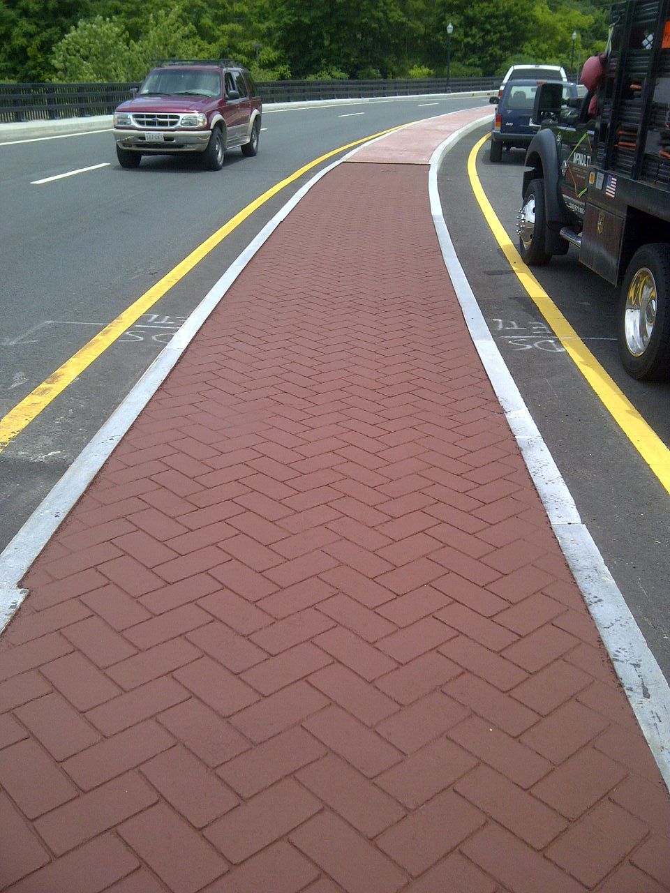 A red truck is driving down a road next to a brick walkway