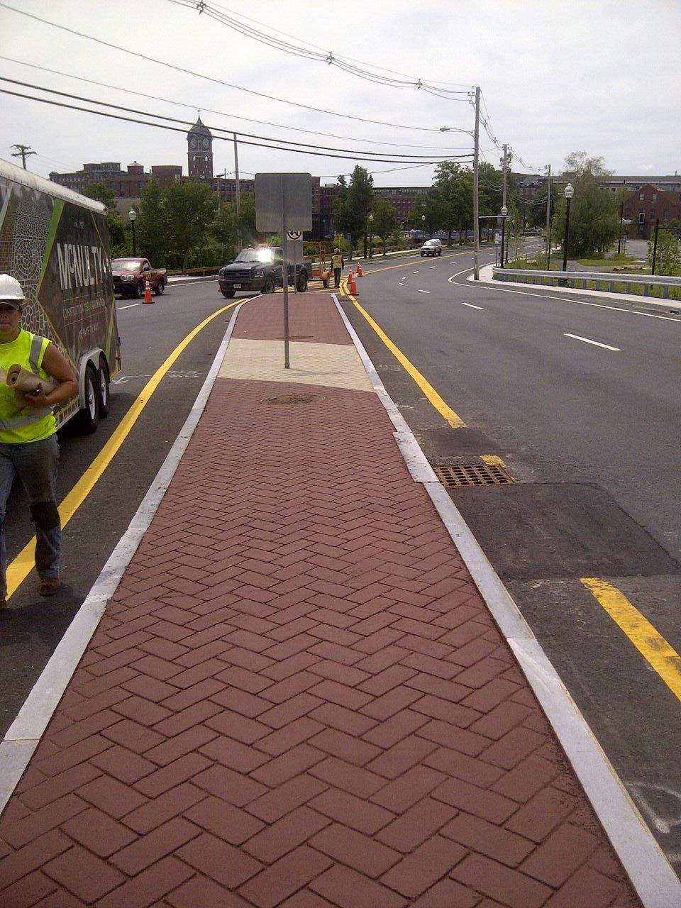 A man in a yellow vest is walking down a brick sidewalk