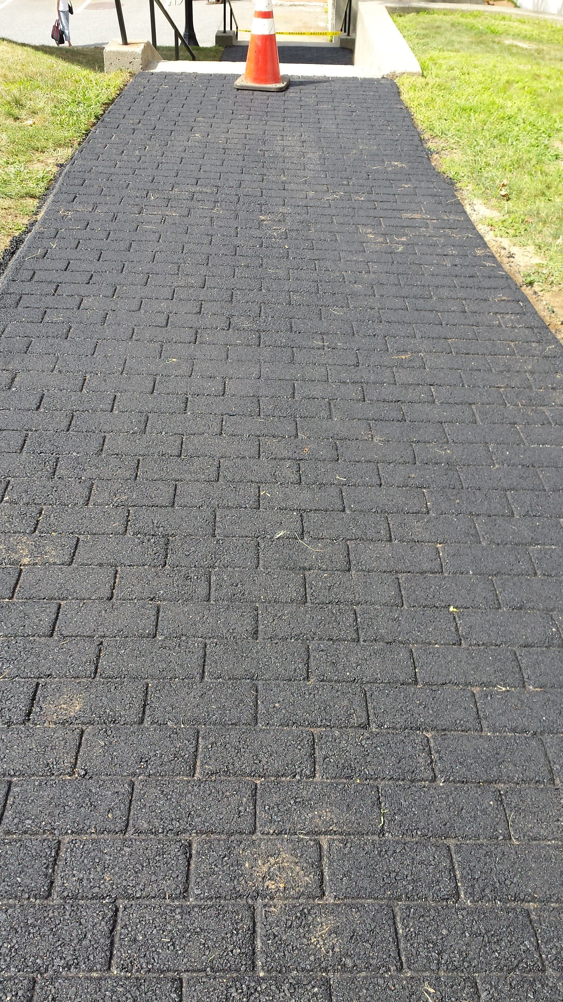 A black walkway with a red cone on the side of it.
