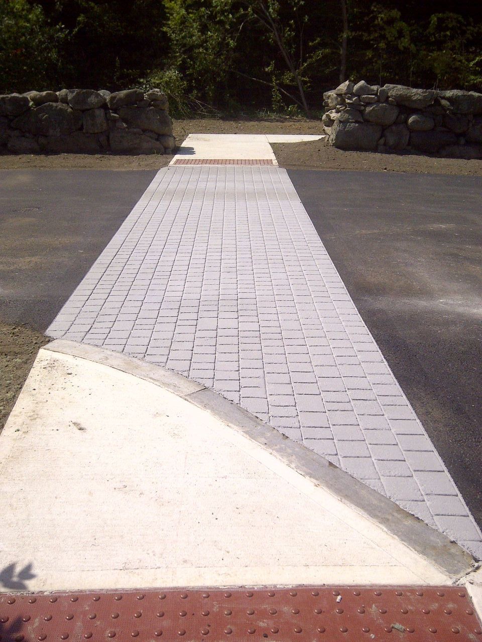 A brick walkway leading to a stone wall with trees in the background.