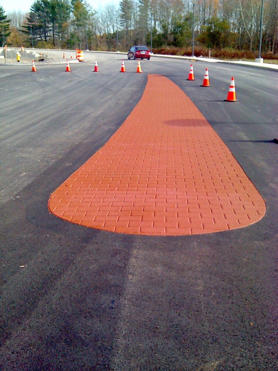 A red car is driving down a road with orange cones
