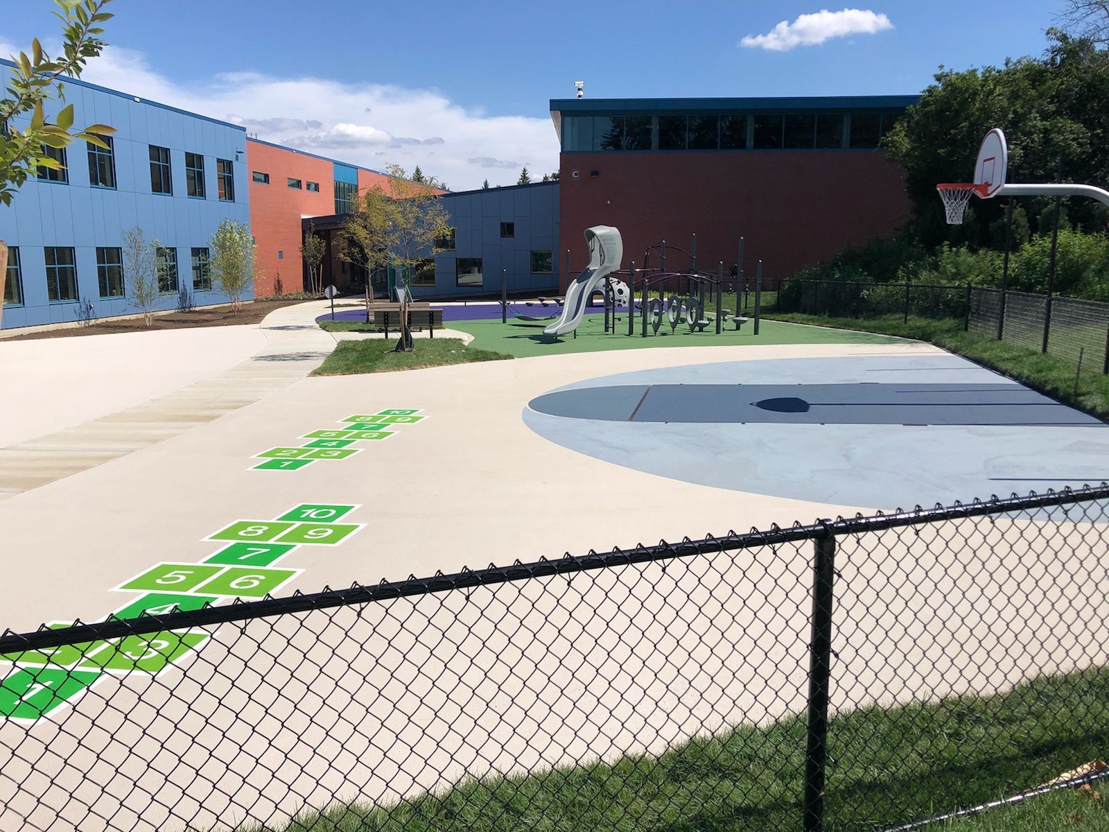 A schoolyard with a basketball court and a playground behind a chain link fence.
