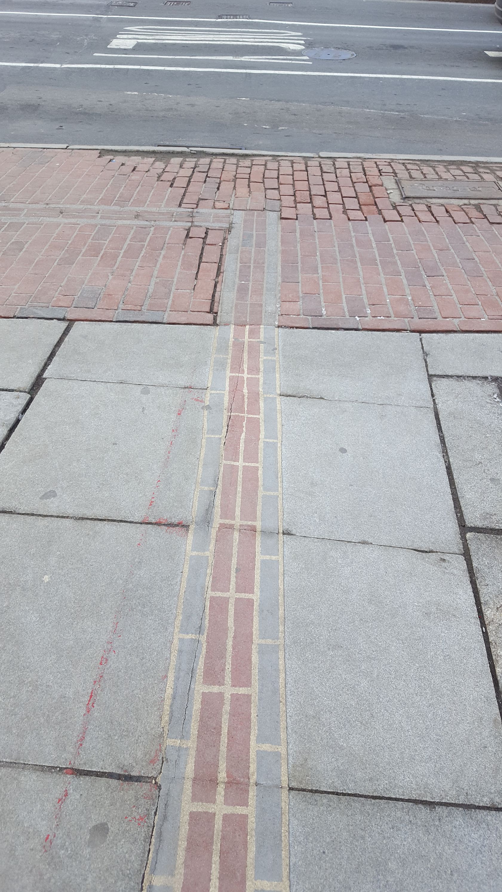 A brick sidewalk with a crosswalk in the background
