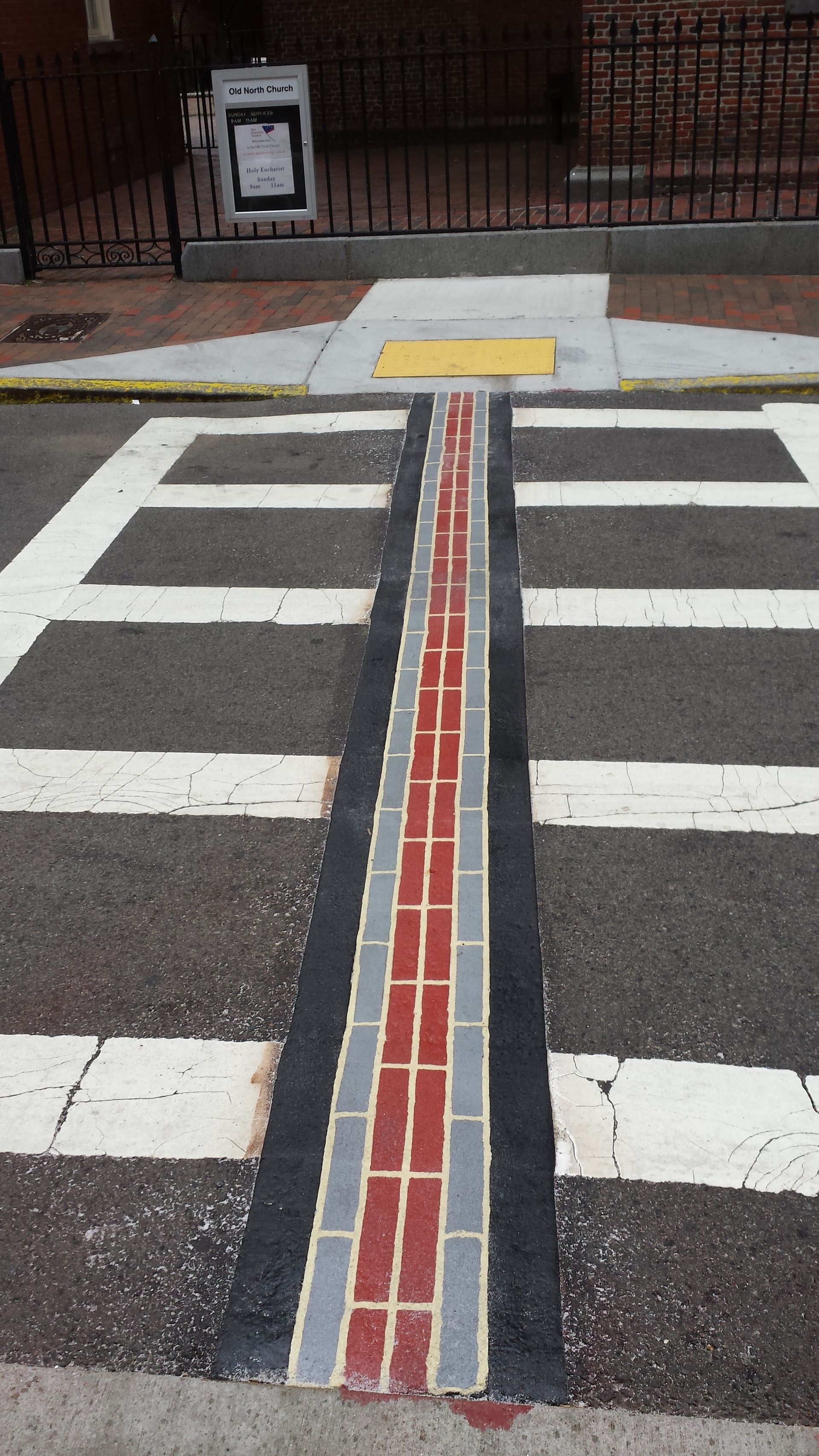 A crosswalk with a brick line in the middle of it