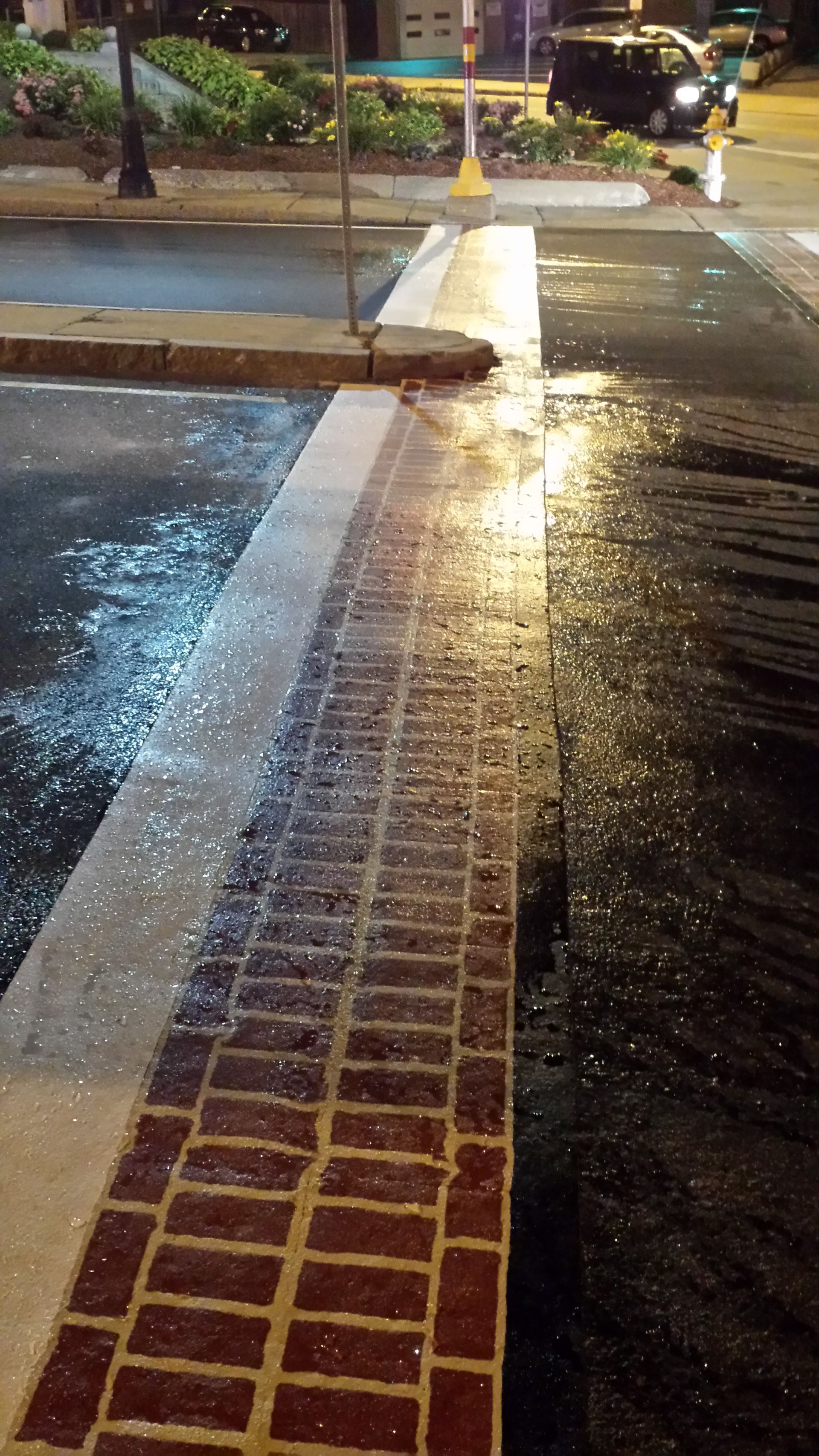 A brick walkway next to a wet street at night