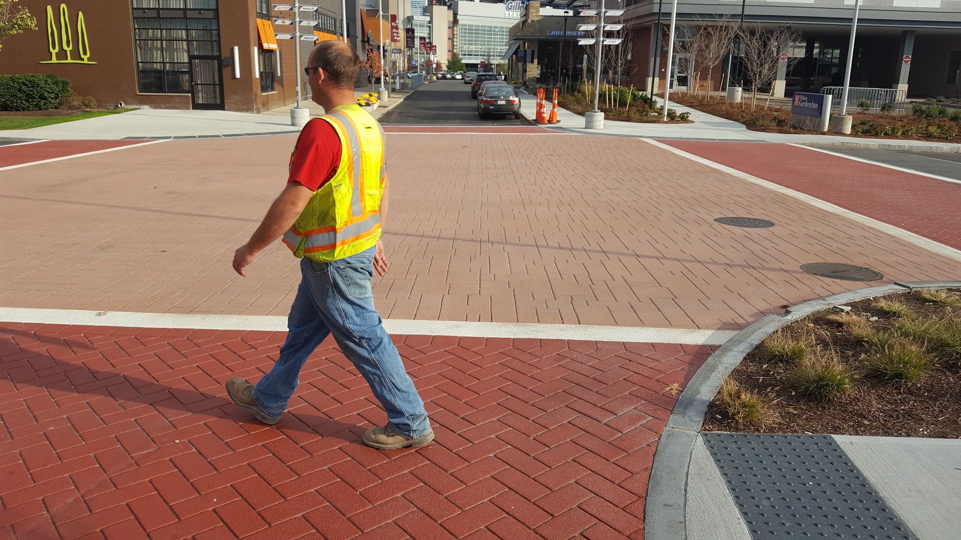 A man in a yellow vest is crossing a street