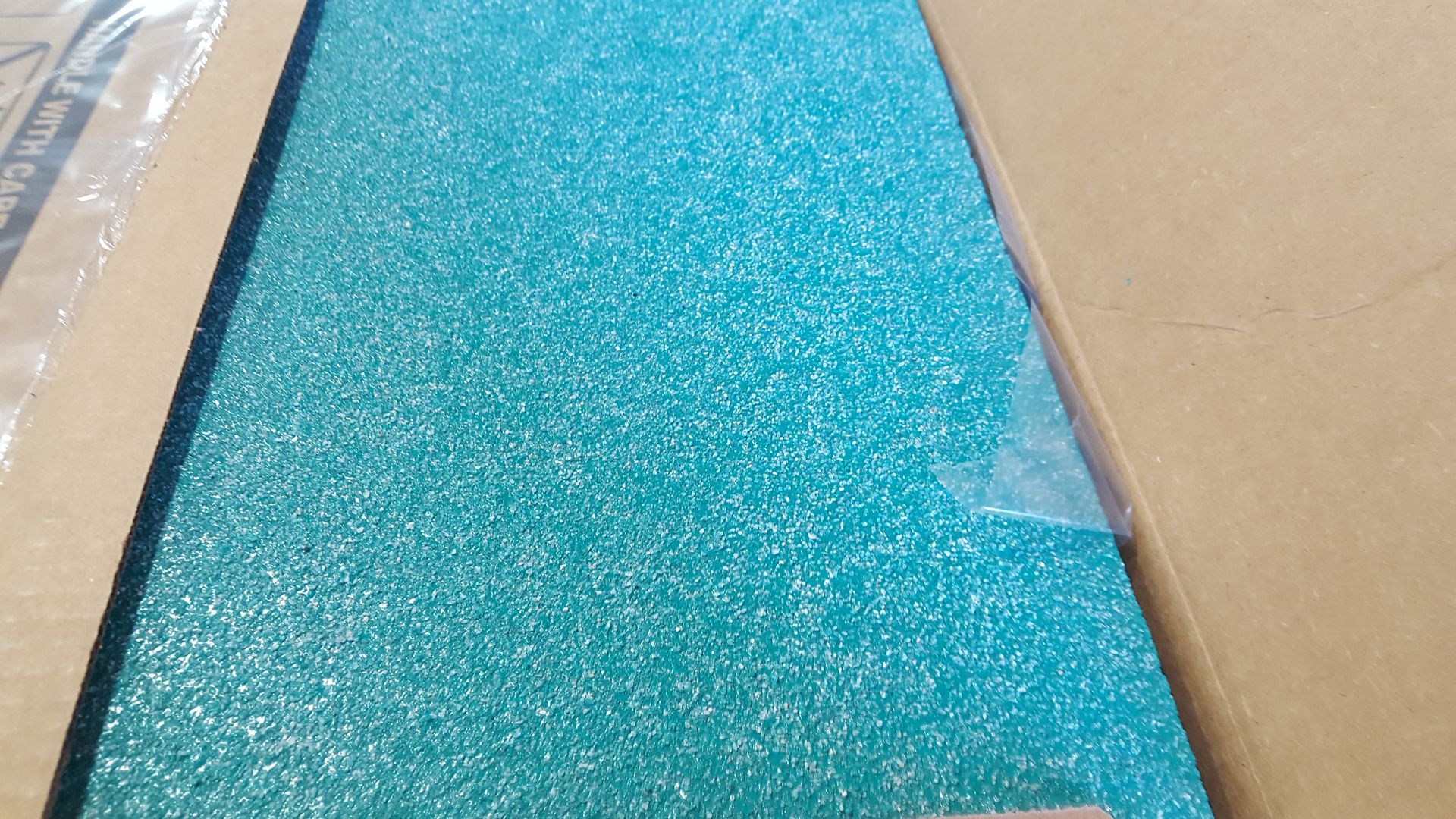 A piece of blue glitter is sitting on top of a piece of cardboard.