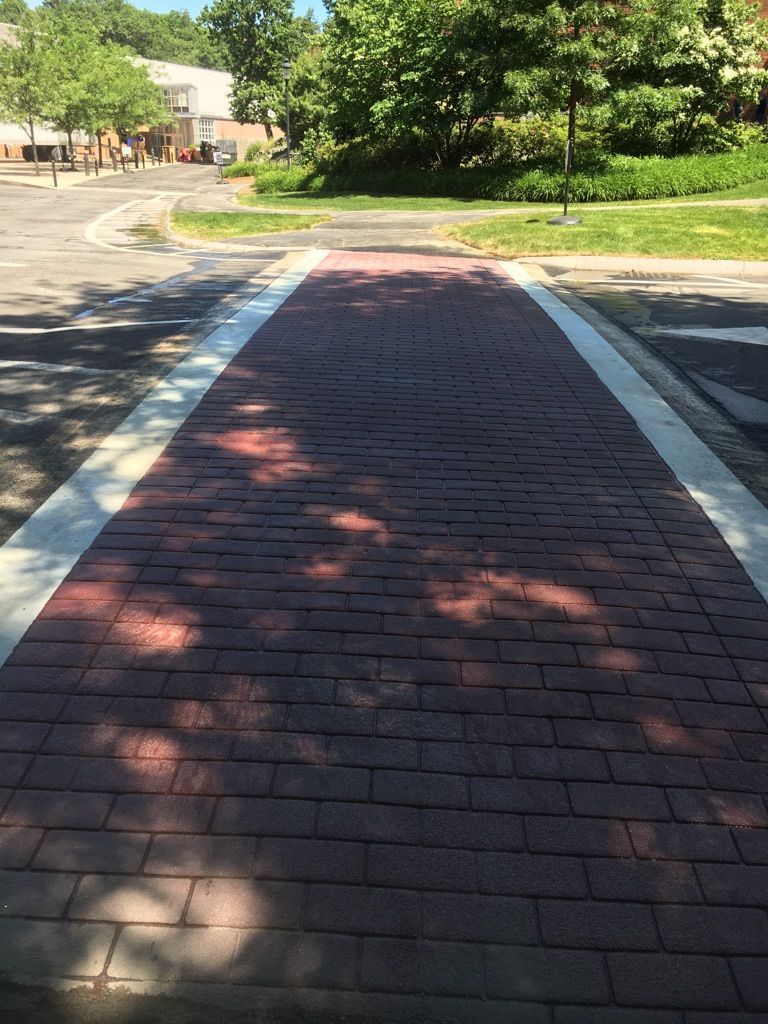 A brick walkway leading to a parking lot with trees in the background.