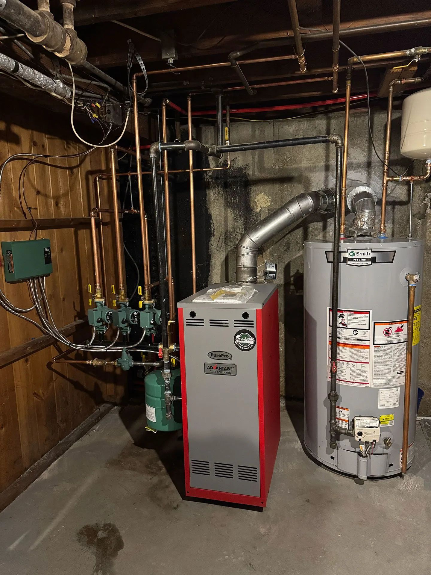 Basement utility room with furnace, water heater, pipes, and exposed wiring.