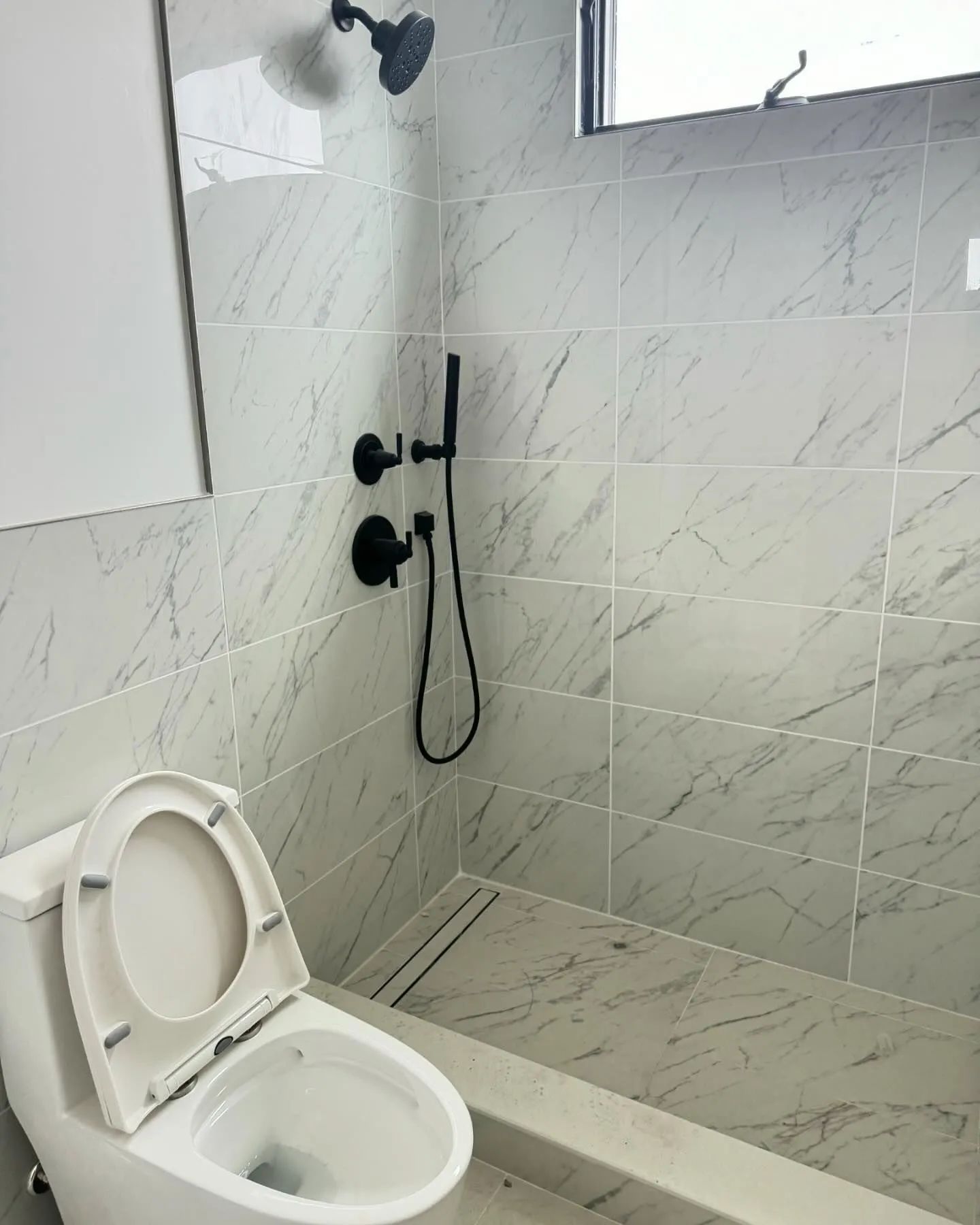 Accessible bathroom with a toilet and black handheld shower on tiled walls and floor.