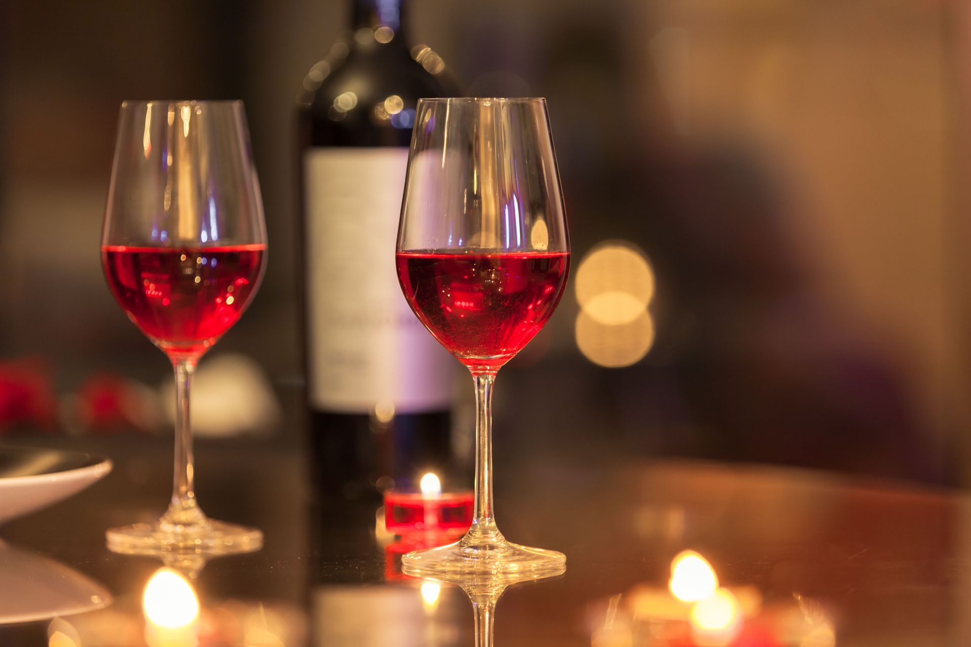 Two glasses of red wine and a bottle of wine on a table with candles.