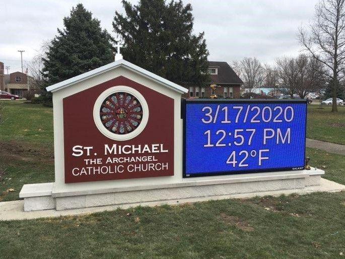 Sign for St. Michael Catholic Church with digital display showing the date, time, and temperature: 42°F.