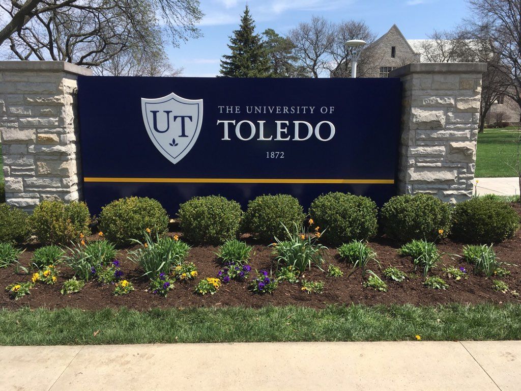 A sign for the university of toledo is surrounded by flowers and bushes