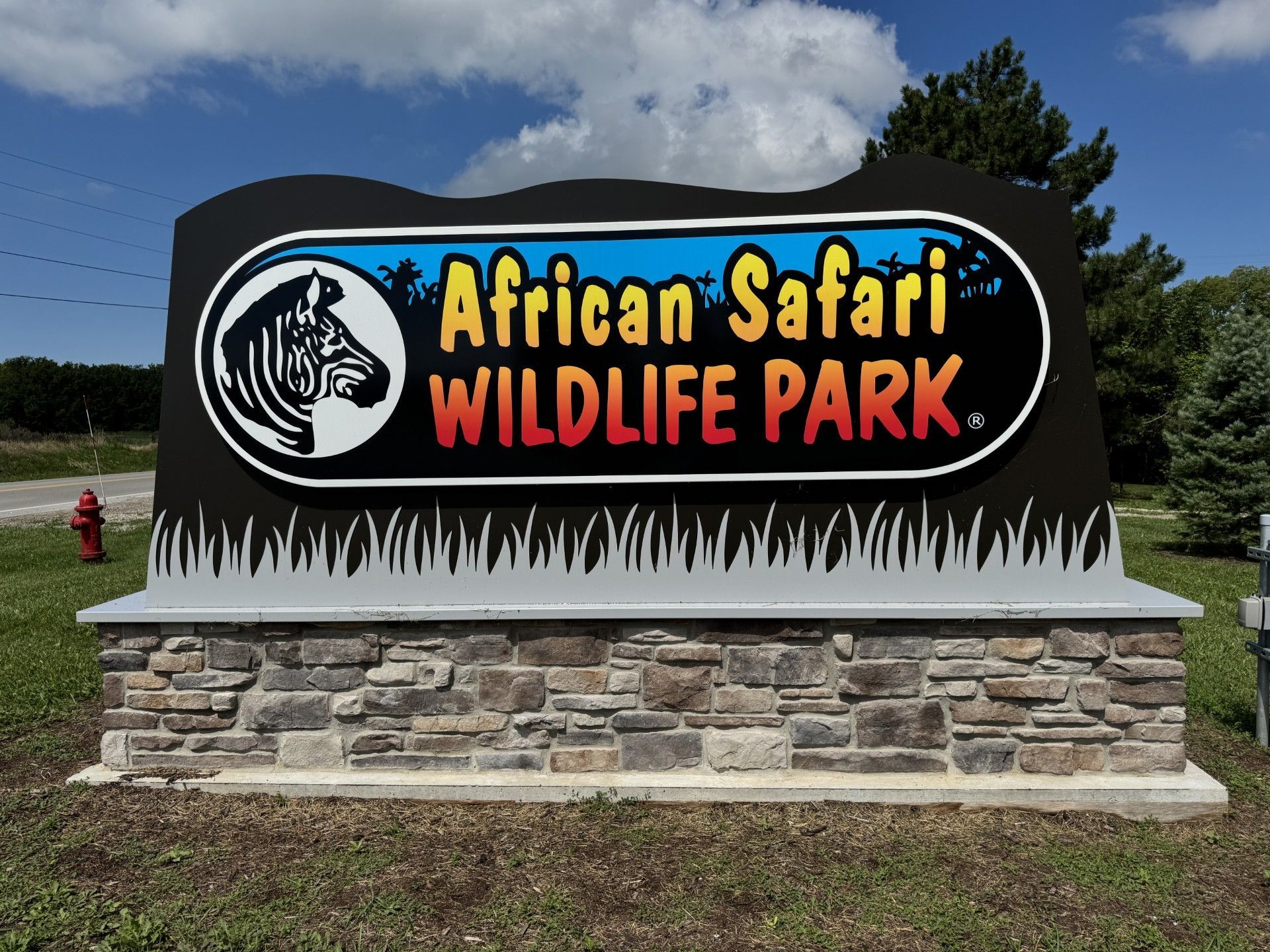 Sign for African Safari Wildlife Park: Zebra emblem, colorful text on black background, stone base.