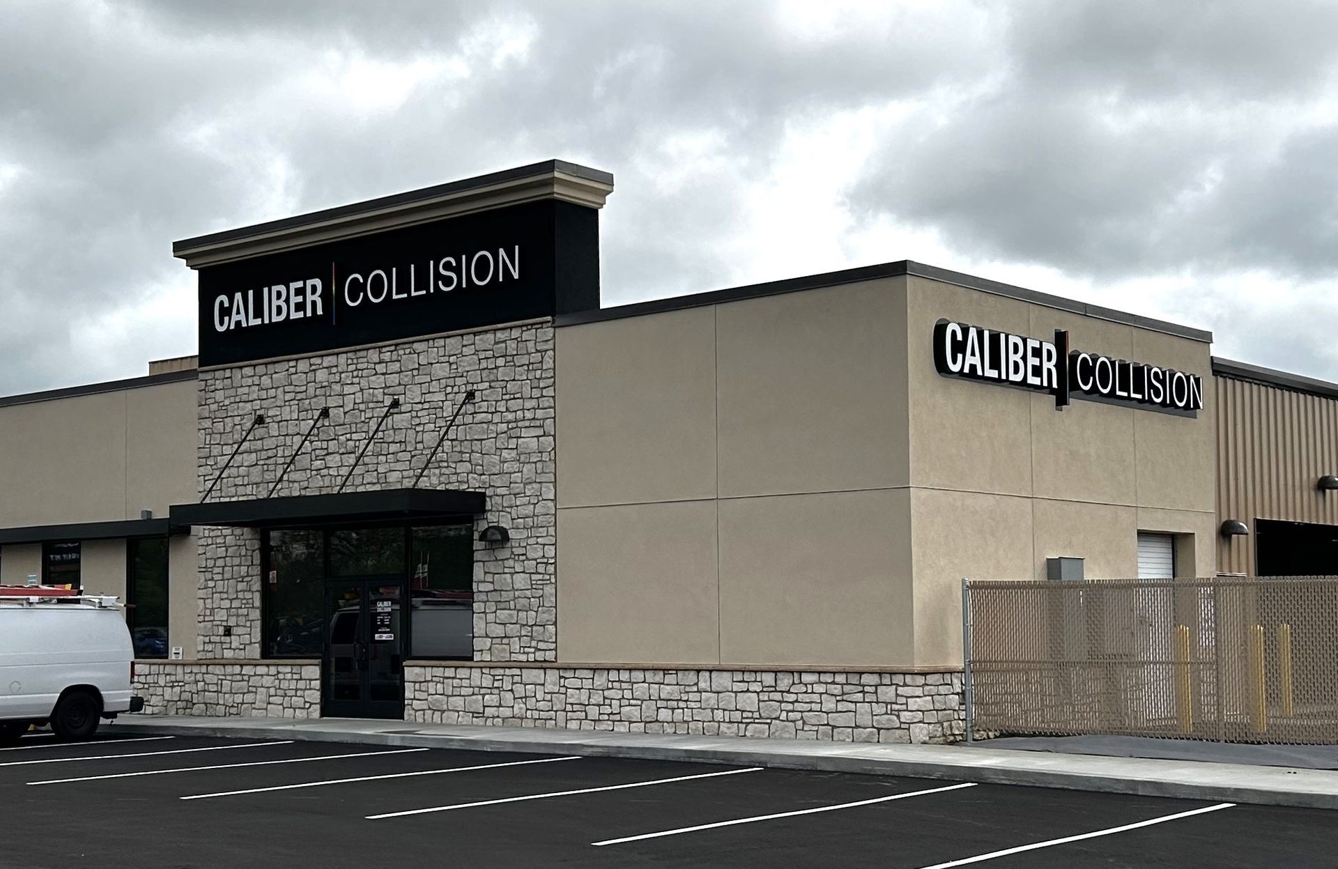 Caliber Collision building with sign on beige building, overcast sky.