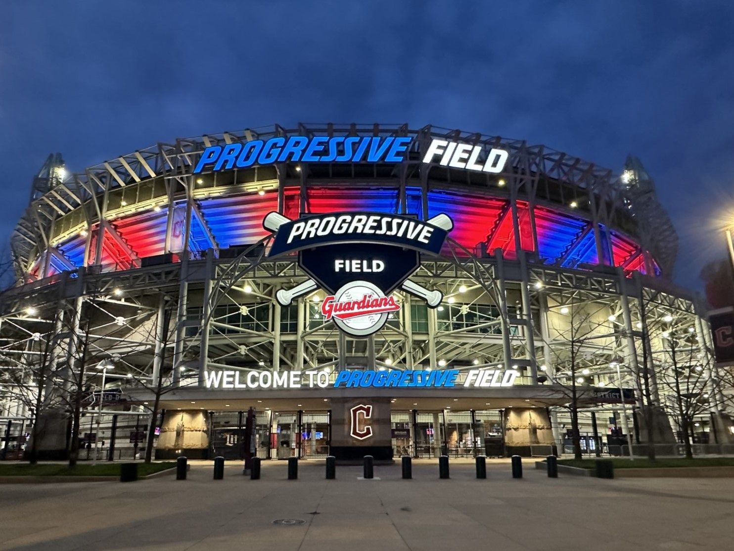 Progressive Field at night lit with red, white, and blue lights; Cleveland Guardians baseball logo.