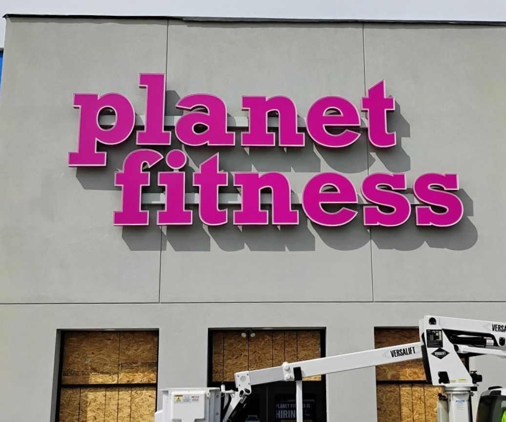 Planet Fitness sign in pink, on a gray building facade; a construction lift is visible.