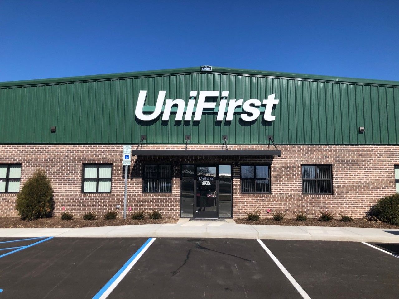 UniFirst building with green metal awning, brick exterior, and clear blue sky.