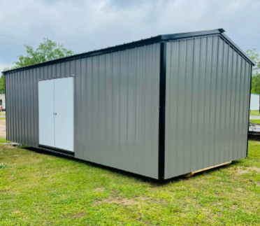 Gray metal storage building with white double doors on a grassy lot