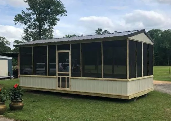Small beige screened porch or sunroom on a grassy lot with trees in the background