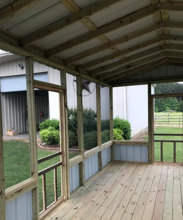 Covered wooden porch with screened windows, railing, and a view of the yard and fence beyond
