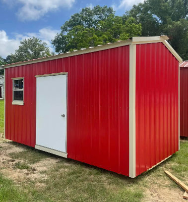 Red metal storage shed with white door and small window, sitting on grass under trees.