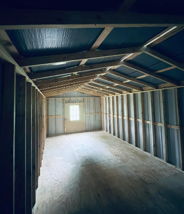 Empty unfinished wooden shed interior with exposed framing and a small window at the far end