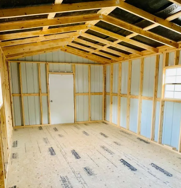 Unfinished room with exposed wooden rafters, insulated walls, a white door, and a subfloor under construction.