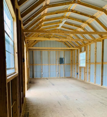 Empty unfinished shed interior with exposed wooden framing, metal walls, and windows along the side.