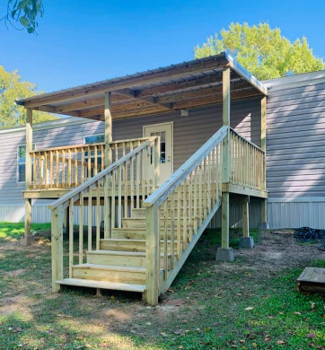 Front porch with wooden stairs and railing on a small cabin, outdoors in daylight.
