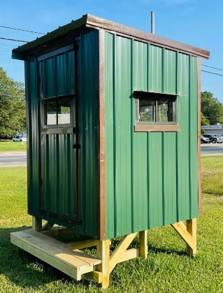 Small green raised wooden shed with windows on a grassy lot under a clear sky