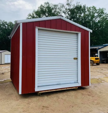 Red storage shed with white roll-up door on a dirt lot