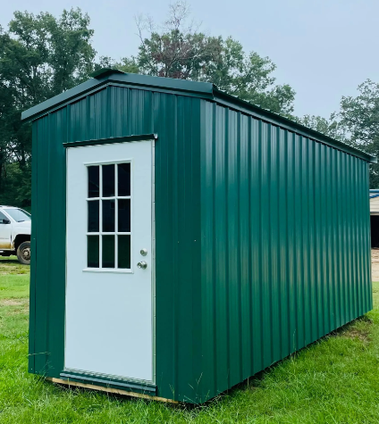Green metal shed with a white door standing on grass outdoors