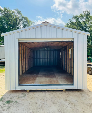 White metal storage shed with a large open front and wooden interior, sitting outdoors on gravel.