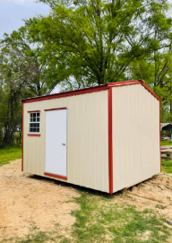 Small beige storage shed with red trim and white door in a grassy, wooded area.