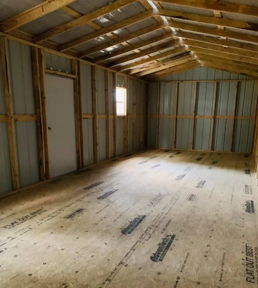 Empty unfinished wooden room with exposed studs, sloped roof, and plywood floor.