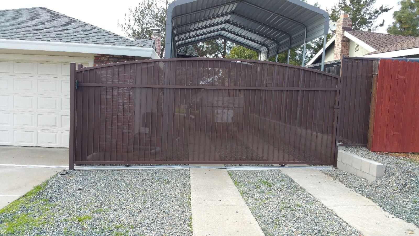 A sliding gate is open to a driveway in front of a house