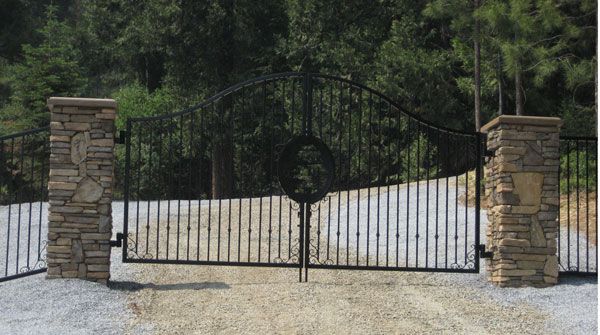 A wrought iron gate is surrounded by stone pillars and trees